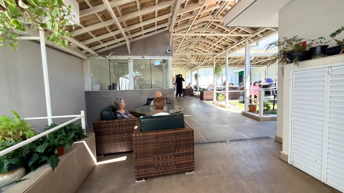 Área de convivência coberta com poltronas de vime e vista para o jardim no Residencial Veneza
