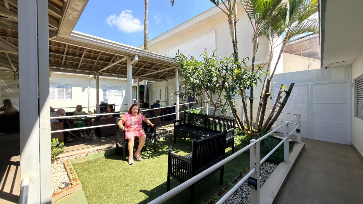 Solarium com bancos e gramado onde idosa descansa no Residencial Veneza