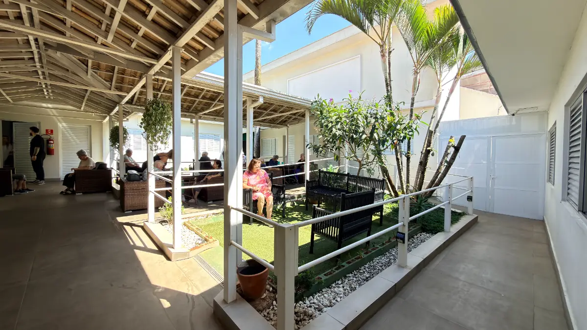 Pátio coberto com jardim interno e bancos onde idosos convivem no Residencial Veneza