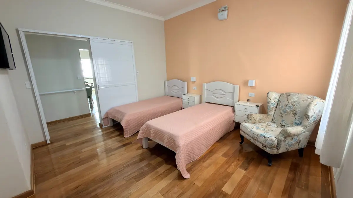 Quarto duplo com poltrona estampada e camas de cabeceira branca no Residencial Veneza